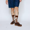 Person wearing brown leather shoes and patterned socks on a white background