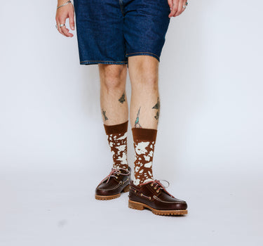 Person wearing brown leather shoes and patterned socks on a white background