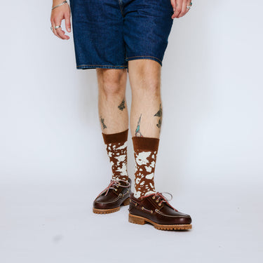 Person wearing brown leather shoes and patterned socks on a white background